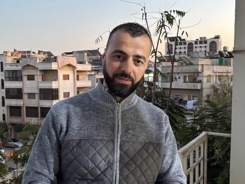 Mann auf Balkon vor Stadtkulisse.