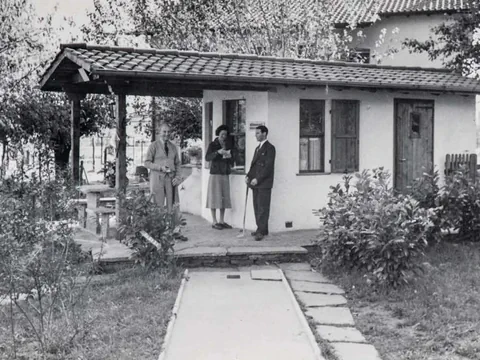 Drei Personen vor einem kleinen Haus mit Garten.