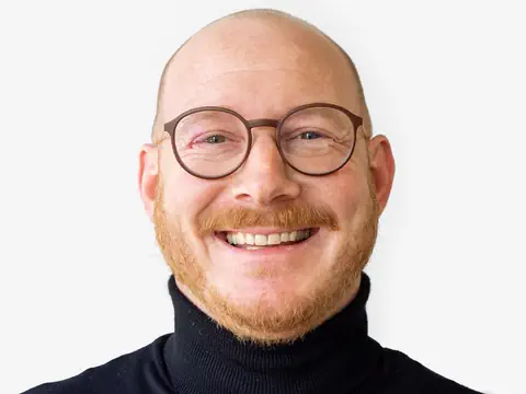 Lächelnder Mann mit Brille und Bart vor weissem Hintergrund.