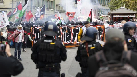 Polizeibeamte stehen vor einer grossen Menschenmenge mit Bannern bei einer Demonstration.