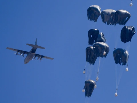 Militärflugzeug mit fallenden Lasten am Fallschirm.
