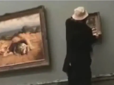 Person in Schwarz hängt kleines Bild neben grosses Gemälde auf.