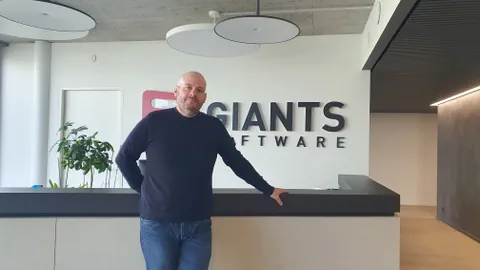 Mann im mittleren Alter und mit Glatze steht vor einer Rezeption, dahinter das Giants-Logo. Er trägt Jeans und Pullover.