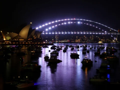 Nachtansicht der Sydney Opera und Hafenbrücke mit beleuchteten Booten.