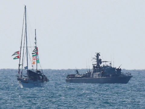Segelboot mit Flaggen neben Marineschiff auf dem Meer.