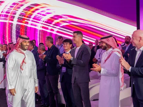 Ein Mann in langem weissem Hemd und rotem Kopftuch geht an applaudierenden Männer vorbei, ua Ronaldo & Gianni Infantino.