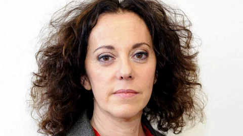 Eine Frau mit braunen Locken, grauem Jacket und rotem Hemd.