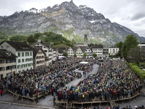 Menschenmenge auf einem Platz in der Schweiz, umgeben von Bergen.