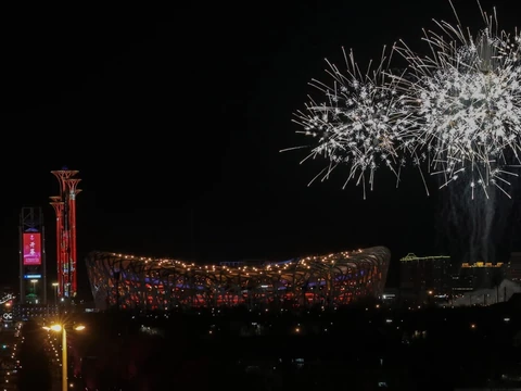 Feuerwerk über beleuchtetem Stadion bei Nacht.