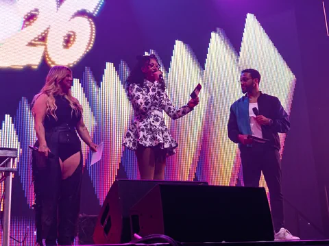 Drei Hosts stehen auf einer Bühne