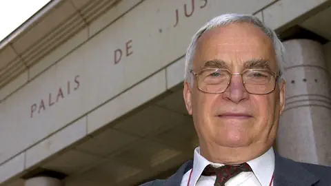 Ein Herr in Anzug und Brille steht vor dem Justizgebäude in Genf.