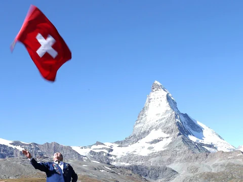 Person schwenkt Schweizer Flagge vor dem Matterhorn.