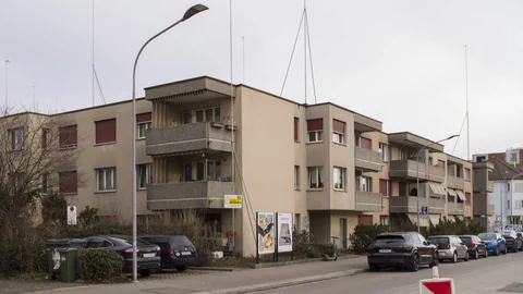 Mehrfamilienhäuser an einer Strasse mit geparkten Autos.