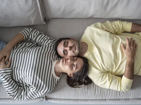 Zwei Menschen, die mit Wangen aneinander auf dem Sofa schlafen.