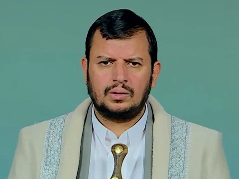 Mann mit traditioneller Kleidung vor grünem Hintergrund.