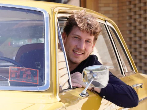 Donat Hofer lehnt sich aus dem Fenster eines gelben Oldtimerautos