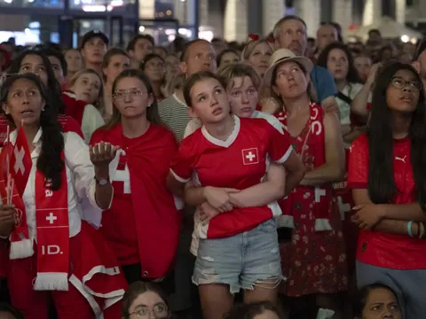 Gruppe von Menschen in roten Fussballtrikots schaut gespannt nach oben.