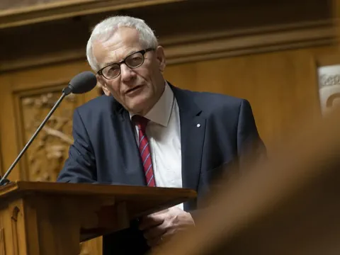 Älterer Mann mit Brille spricht an einem Holzpult.