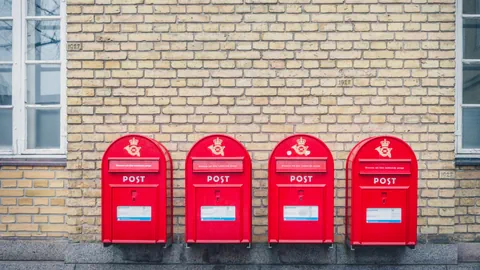 Vier rote Briefkästen an einer Hauswand.