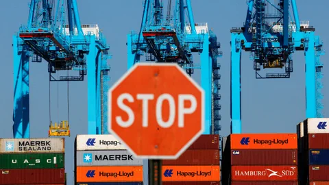 Stopp-Schild vor Containern und Kränen im Hafen.