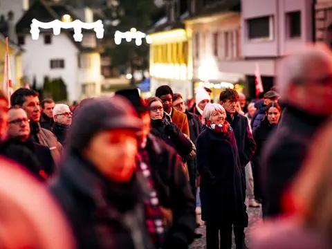 Menschenmenge auf einer nächtlichen Strasse mit Lichtern im Hintergrund.