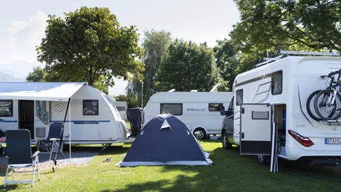 Wohnmobile und Zelt auf einem Campingplatz mit Bäumen im Hintergrund.