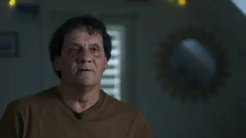 Mann in braunem Shirt in dunklem Raum.