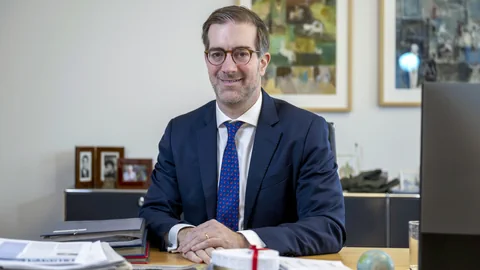 Conradin Cramer sitzt am Bürotisch und schaut in die Kamera.