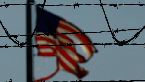 Verschwommene US-Flagge hinter Stacheldraht im Wind.