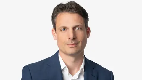 Person in einem blauen Anzug vor weissem Hintergrund.