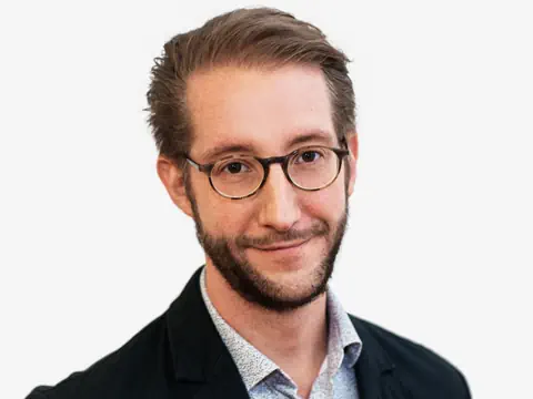 Mann mit Brille und Bart vor weissem Hintergrund.