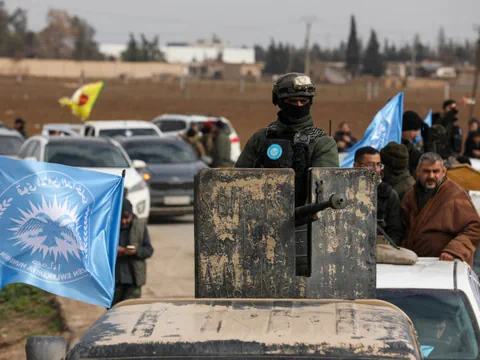 Bewaffnete Person auf Fahrzeug mit Flaggen in Hintergrund.