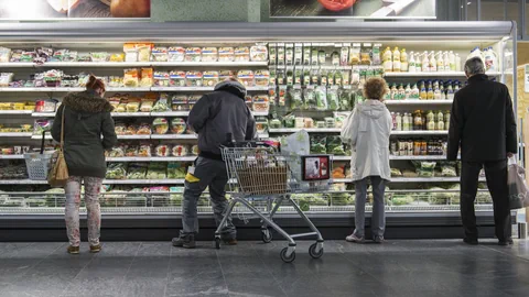 Vier Personen stehen vor einem Kühlregal im Supermarkt.