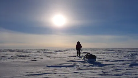 Frau läuft mit Skiern und Schlitten durch eine Schneelandschaft und zieht einen Schlitten hinter sich her.