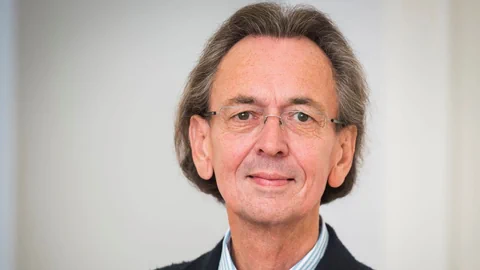 Mittelalter Mann mit kinnlangen Haaren trägt eine Brille und lächelt leicht in die Kamera.