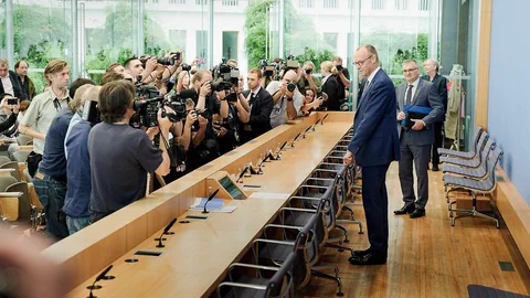 Pressekonferenz mit Fotografen und Sprechern in einem Raum.