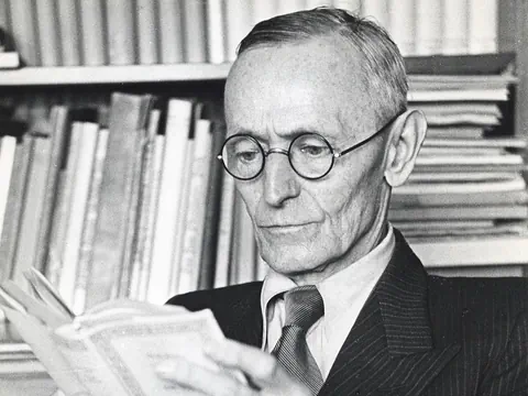 Mann mit Brille liest Buch vor Bücherregal.