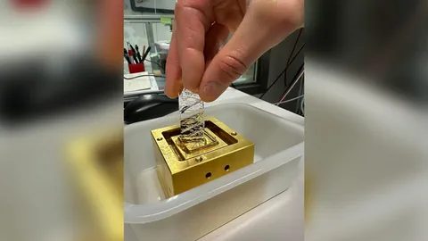 Eine Hand hält Metallstreifen über einen goldenen Apparat.