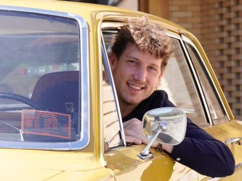 Donat Hofer lehnt sich aus dem Fenster eines gelben Oldtimer Autos