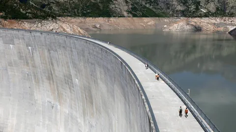 Menschen gehen über eine grosse Staumauer.