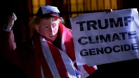 Eine Person mit einer Trump-Maske hält ein Schild mit der Aufschrift «Trump Climate Genocide»