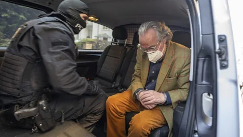 Reuss mit Handschellen in einem Auto, ein Polizist bei ihm.