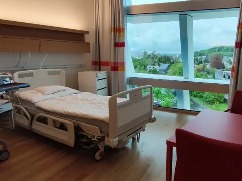 Krankenhauszimmer mit einem Bett und Blick auf die Landschaft.