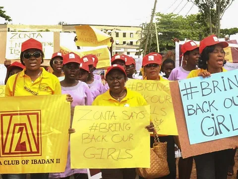 Gruppe von Menschen in gelber und lila Kleidung mit Schildern bei einer Demonstration.