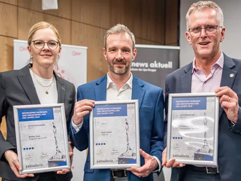 Drei Personen halten Urkunden bei einer Preisverleihung.