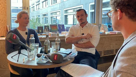 Ein Mann sitzt einem Mann und einer Frau in einem Cafe gegenüber.