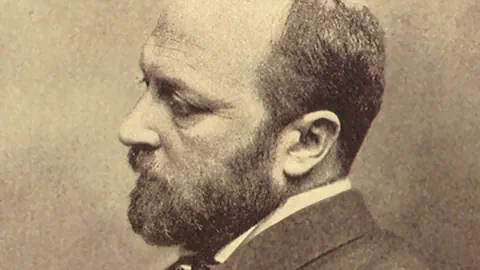 Ein Mann mit Vollbart und Glatze von der Seite aufgenommen.