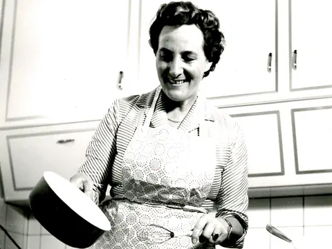 Frau lächelt beim Kochen in der Küche.