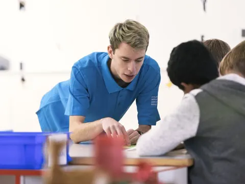 Mann in blauem Hemd berät Kinder am Tisch.