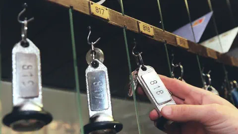 Eine Hand nimmt einen Hotelschlüssel von eibnem Haken.